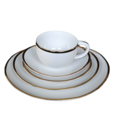 A stack of differently sized oval plates with gold rims. On top is a gold rimmed coffee mug.