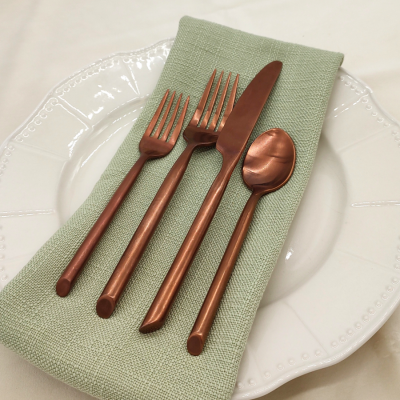 Capri Brushed Copper flatware on a place setting with a green napkin, white plate, and white tablecloth.