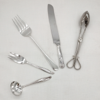Silver serving utensils on a white background. Clockwise, there is a gravy ladle, 8" serving fork, 12" serving fork, serving knife, and salad tongs.