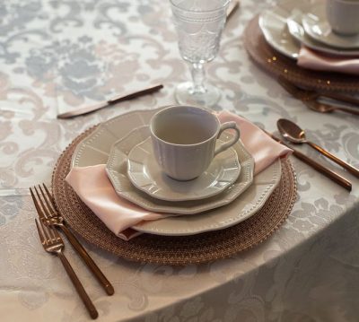 A place setting with white linens, copper napkins and flatware, and Provence plates and cup.