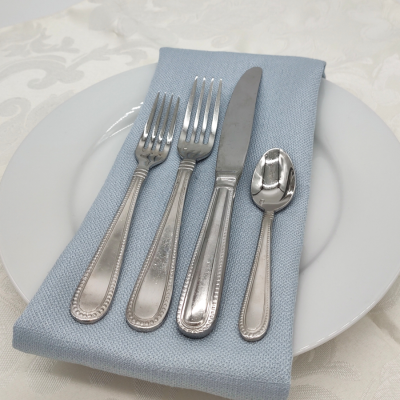 Caviar Stainless Flatware on a place setting with a blue napkin, white plate, and white lace tablecloth.