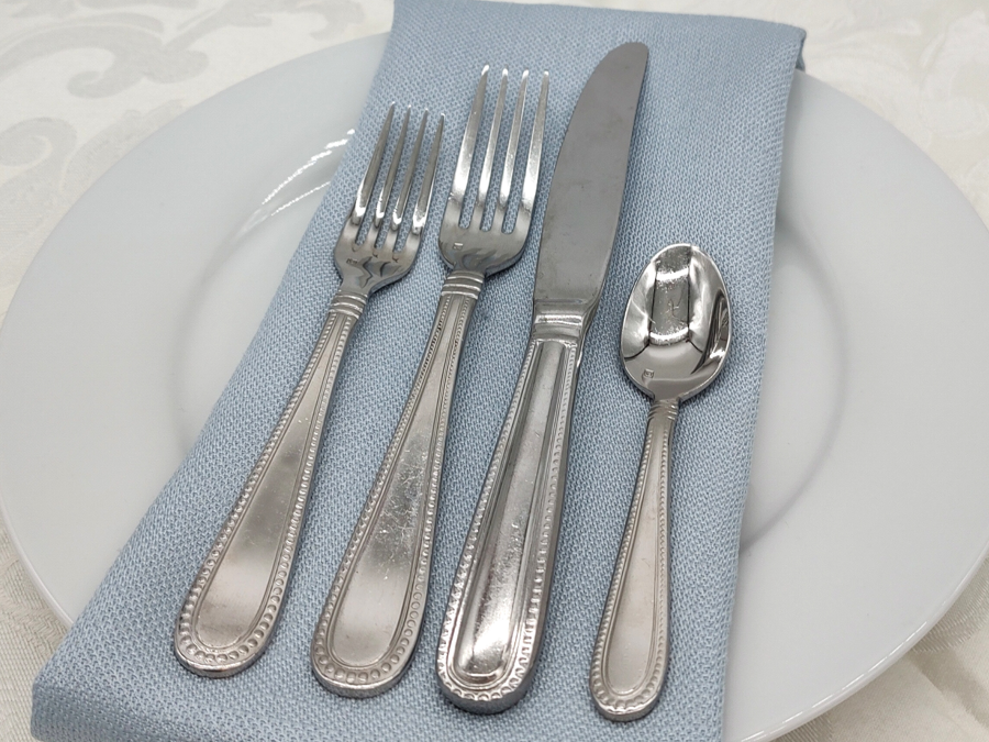 Caviar Stainless Flatware on a place setting with a blue napkin, white plate, and white lace tablecloth.