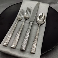 Doria Stainless flatware on a place setting with a silver napkin, black plate, and silver tablecloth.