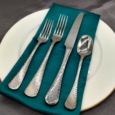 Hammered Stainless flatware on a place setting with a teal napkin, white plate, and gray tablecloth.