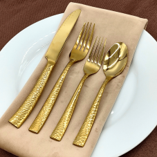 Oxford gold flatware on a place setting with a tan napkin, white plate, and brown tablecloth.