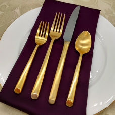 Parker Brushed Gold flatware on a place setting with a brown napkin, white plate, and yellow tablecloth.