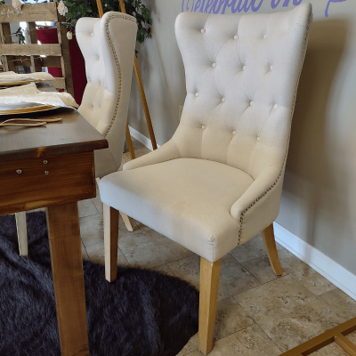 A chair upholstered in light grey fabric. It has wooden legs and a curved back.