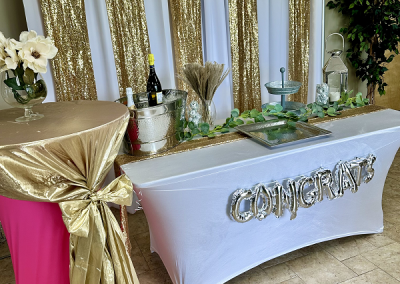 Birthday celebration with high top table in spandex pink and lame gold, and a buffet table in white and gold, with a pipe and drape backdrop in gold lame.